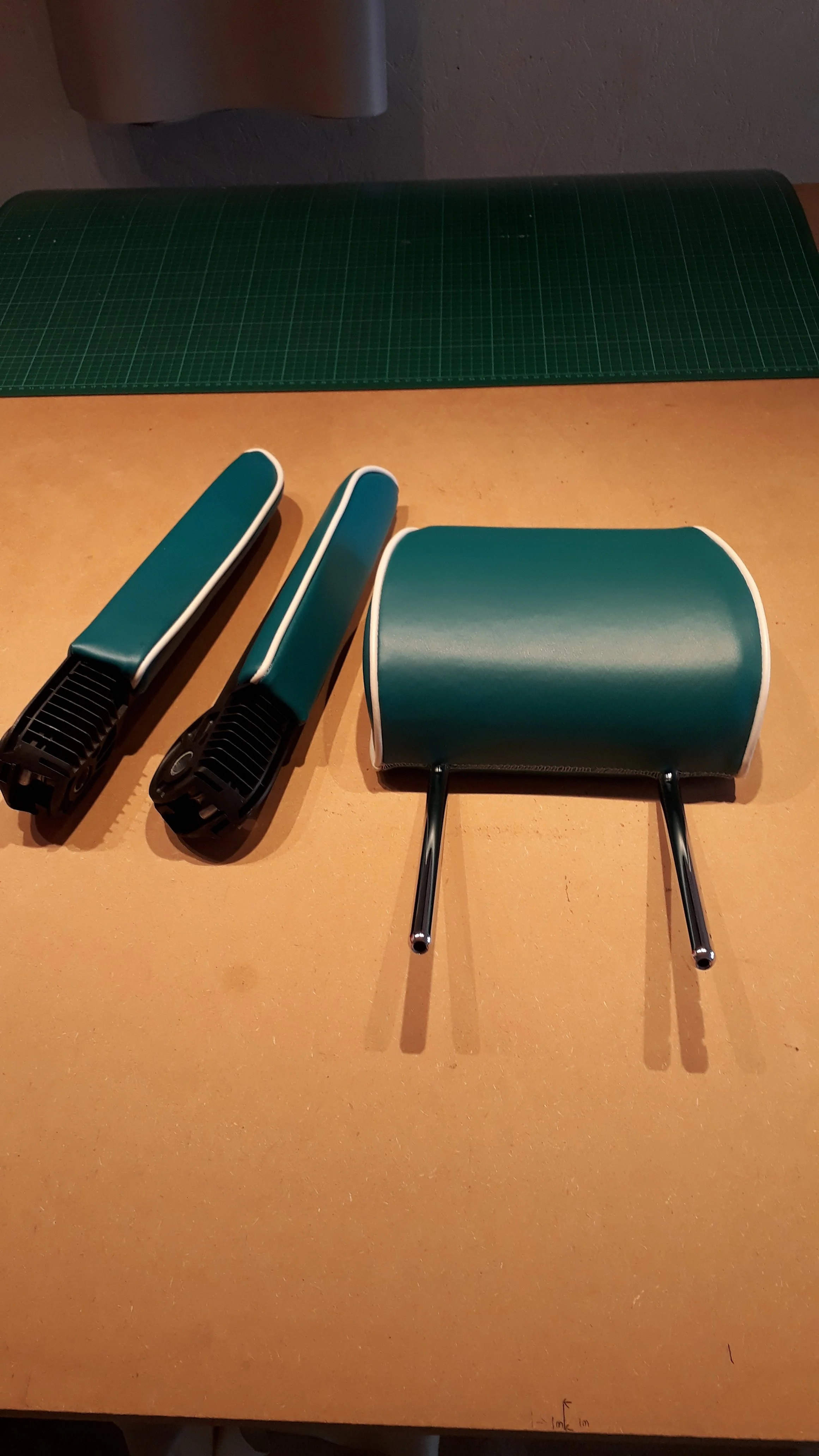 A green cutting mat, two handheld fabric or material steamers, and a green cushioned chair with metal legs on a wooden table.