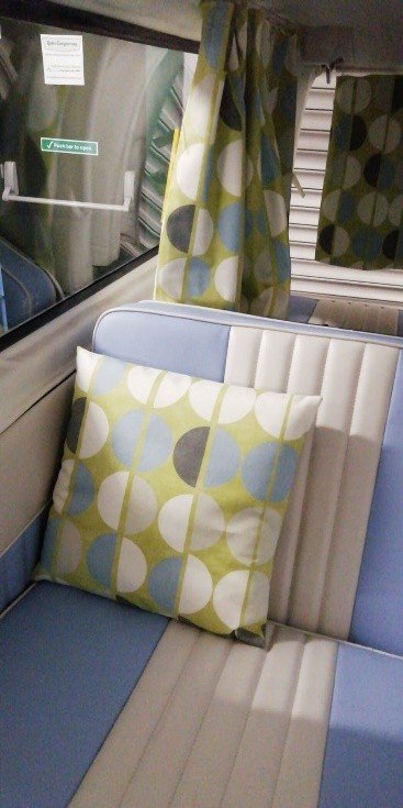 Inside a train or bus, showing a seat with a cushion and curtains with matching geometric circle patterns.