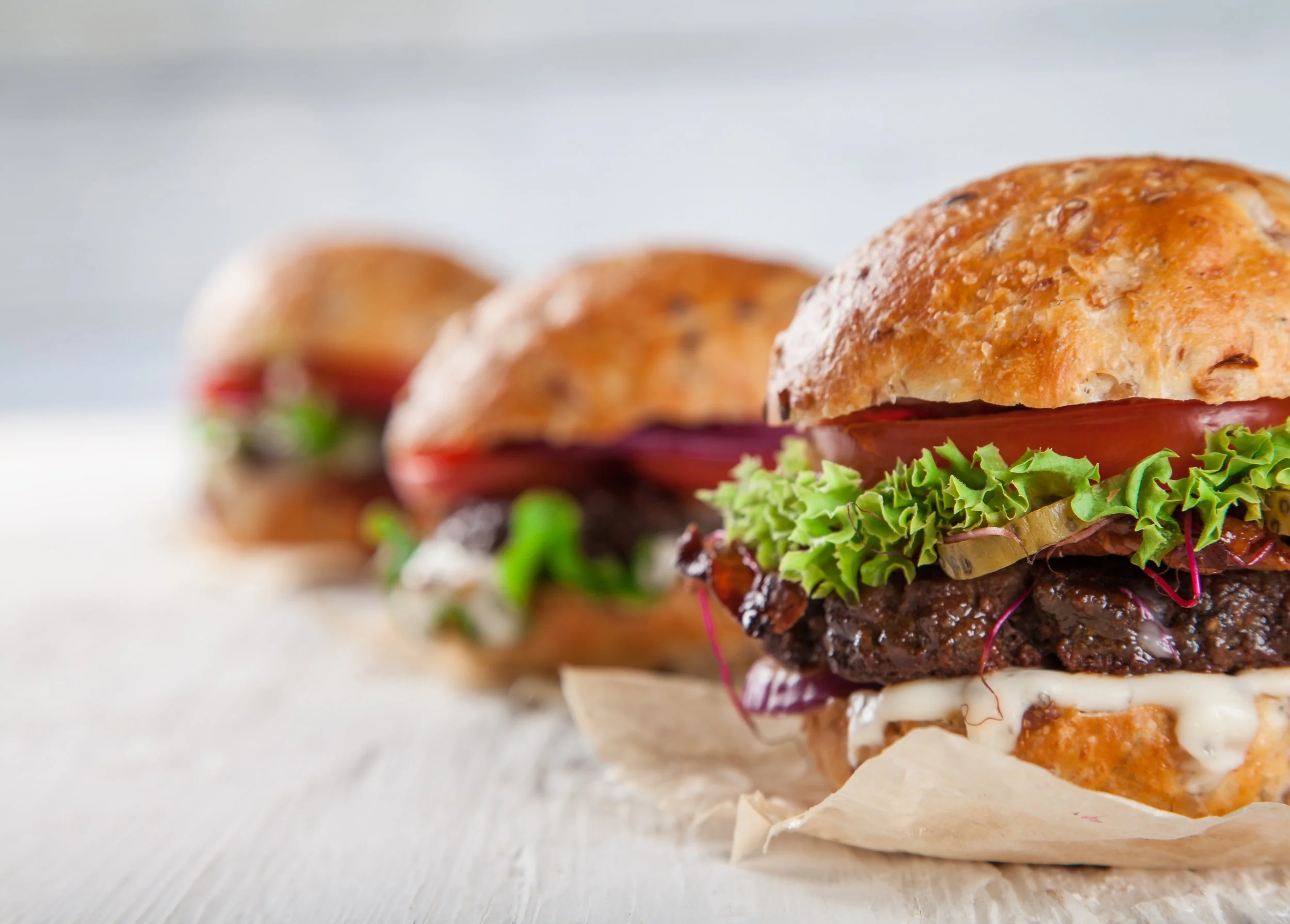 Close-up of a provocative burger with a variety of ingredients, including lettuce, tomato, pickles, and sauces, wrapped in paper on a wooden surface.