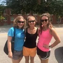 Three young women posing outdoors, all wearing sunglasses and casual summer clothes
