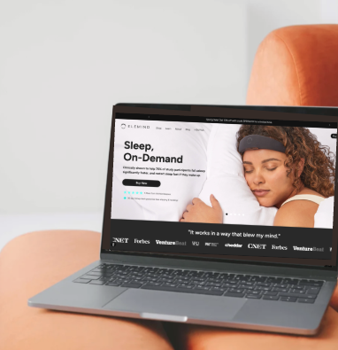 Laptop on a wooden table displaying a website about sleep and on-demand content, with a woman sleeping on the screen. An orange chair is in the background.