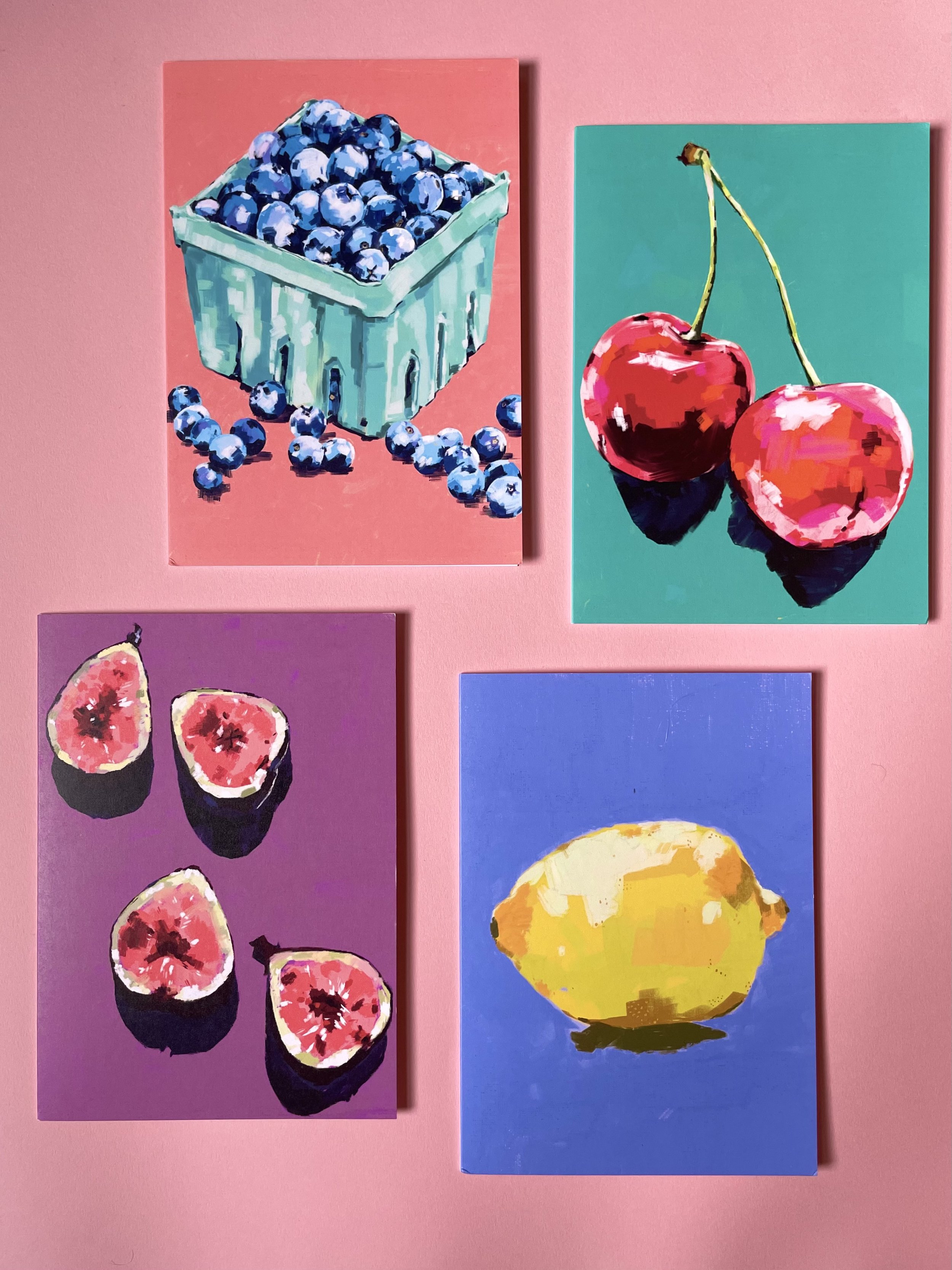 Paintings of blueberries in a basket, cherries, figs, and a lemon on a pink background.