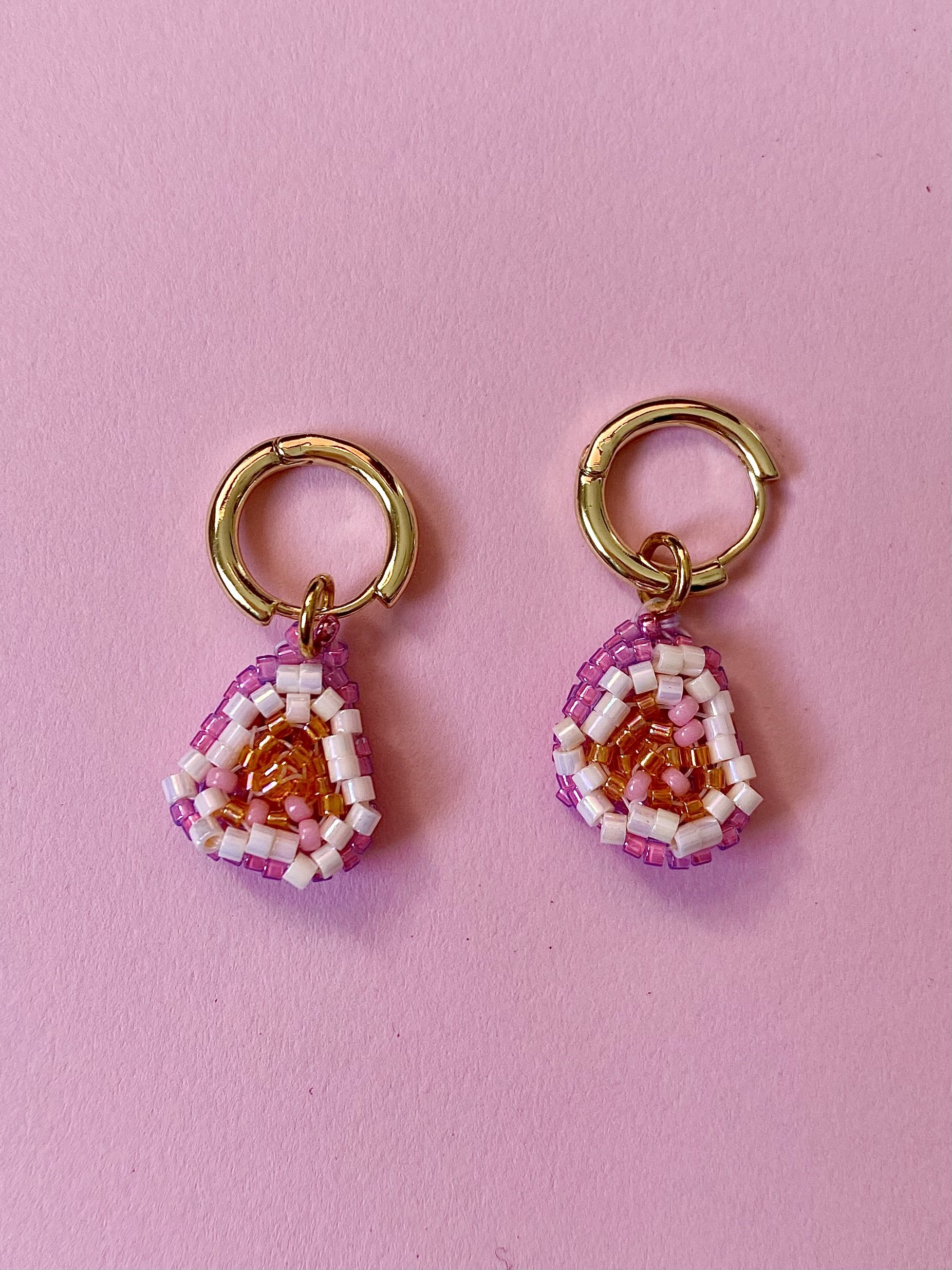 Beaded earrings with gold hoops on a pink background.