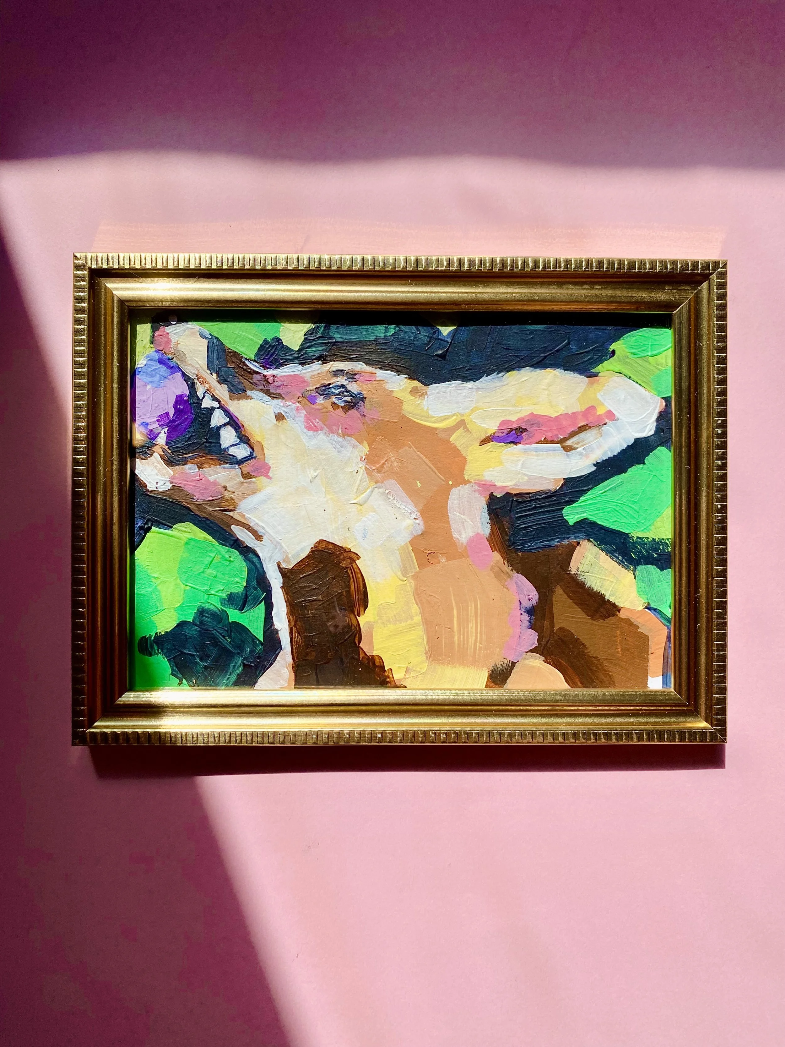 A colorful abstract painting in a gold frame hanging on a pink wall.