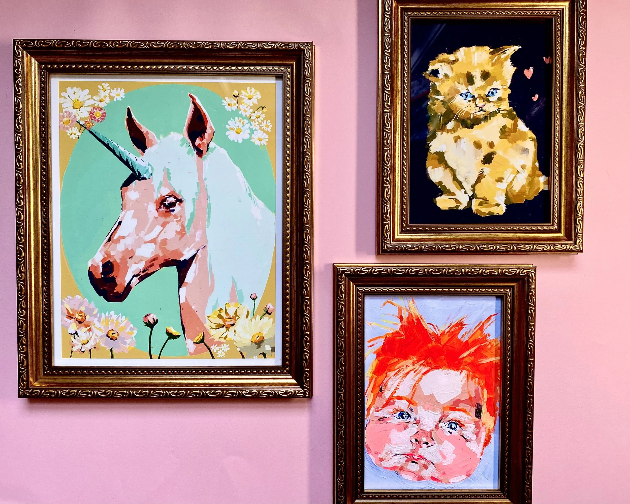 Two framed paintings on a pink wall. The left painting depicts a colorful, abstract illustration of a dog with flowers, and the right painting shows an abstract image of a lion with a dark background.