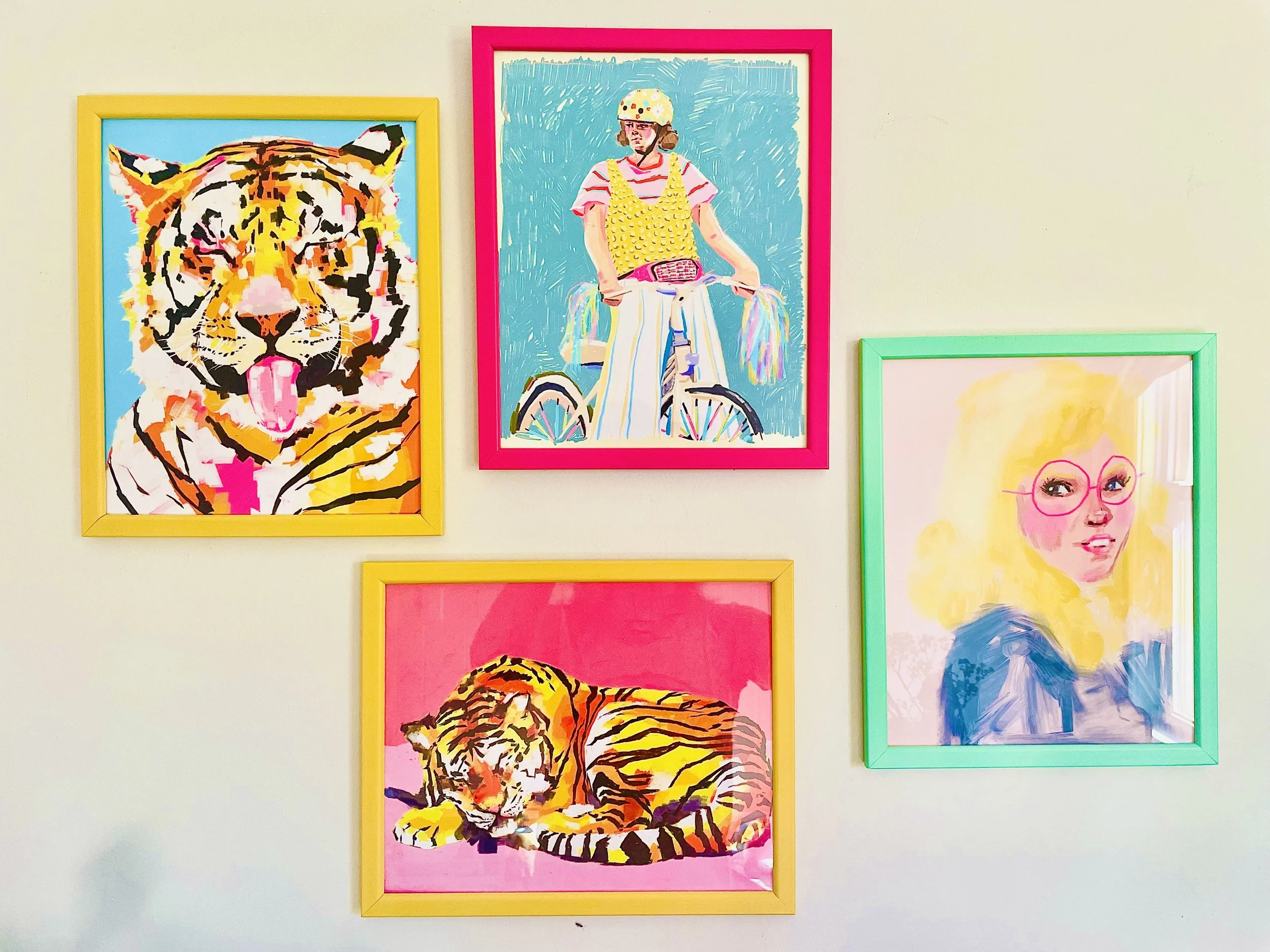 Colorful wall art featuring a tiger, a girl riding a bicycle with a rainbow-colored handlebar, and a girl with glasses, all framed in bright yellow, pink, and green frames.