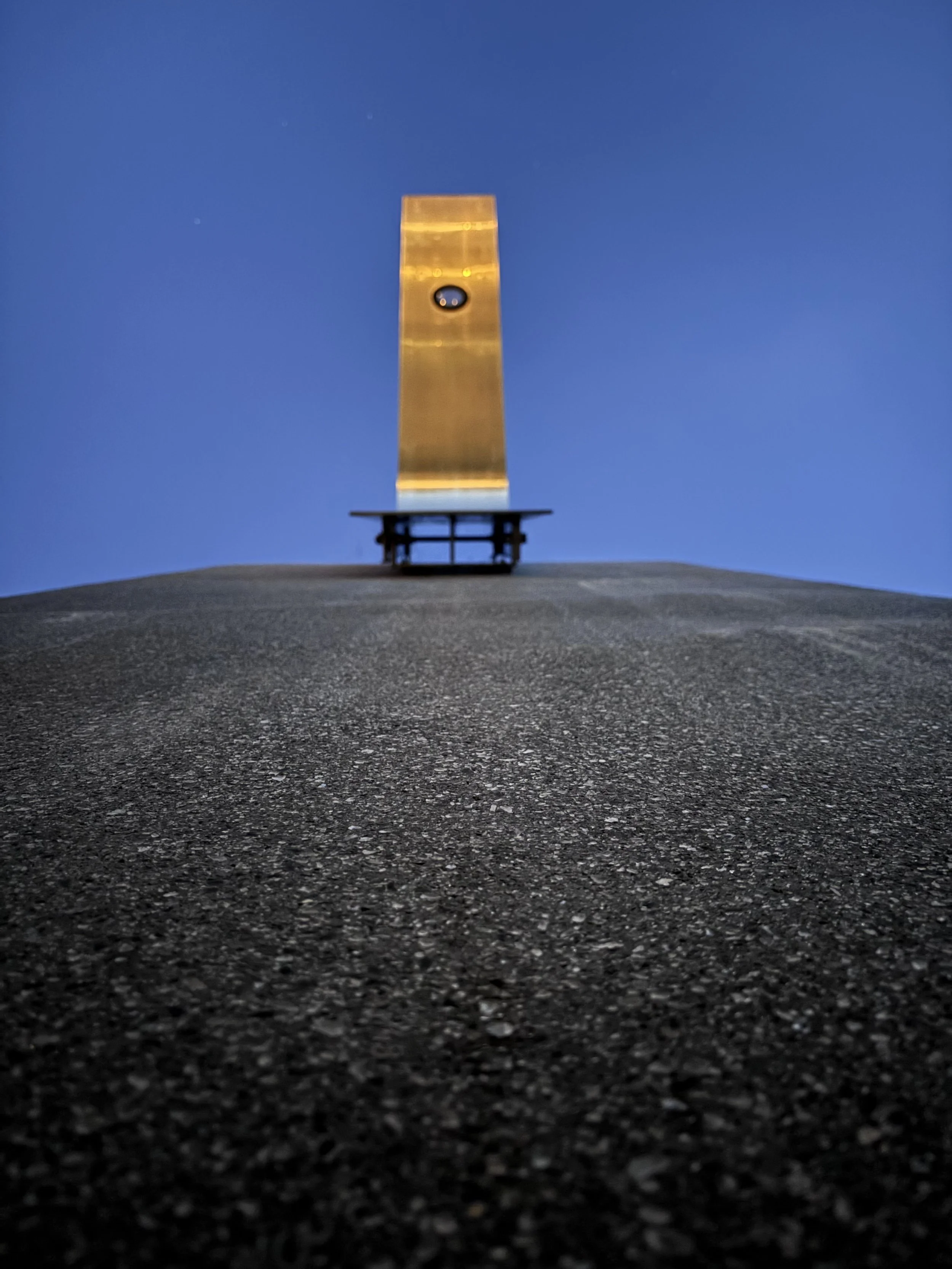 A tall, illuminated obelisk-shaped monument atop a small black platform, set against a darkening sky at dusk, with some stars visible.