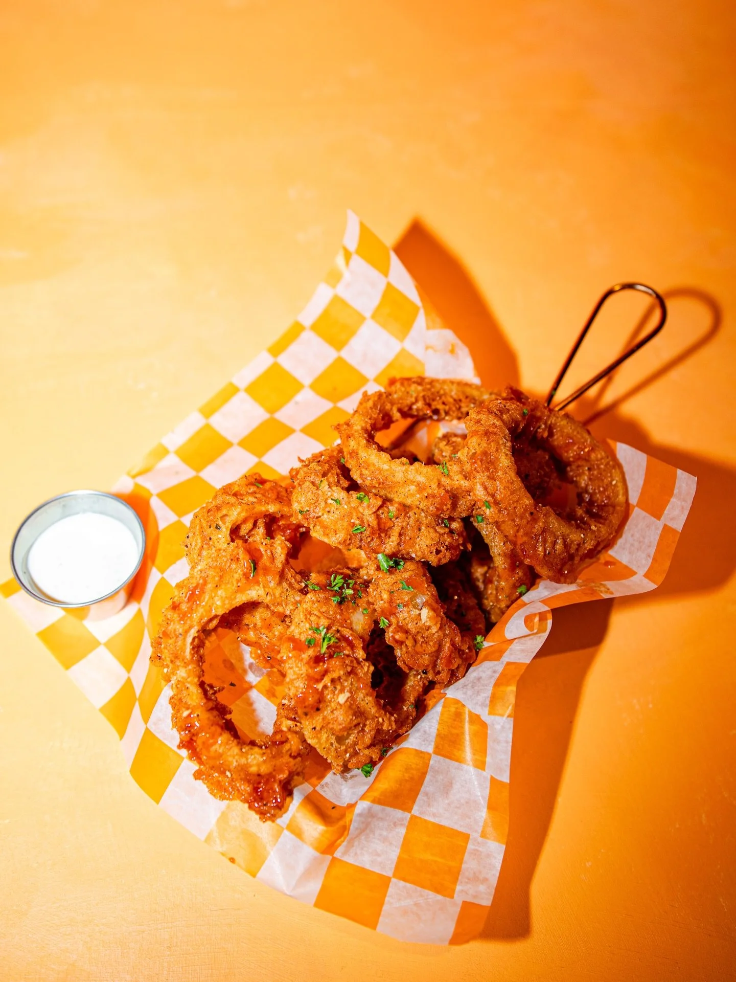 Fried onion rings served with a side of dipping sauce on a checkered paper in a basket.