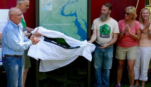 Group of people unveiling a sign at a Potomac Connections event, with trees and a map in the background.