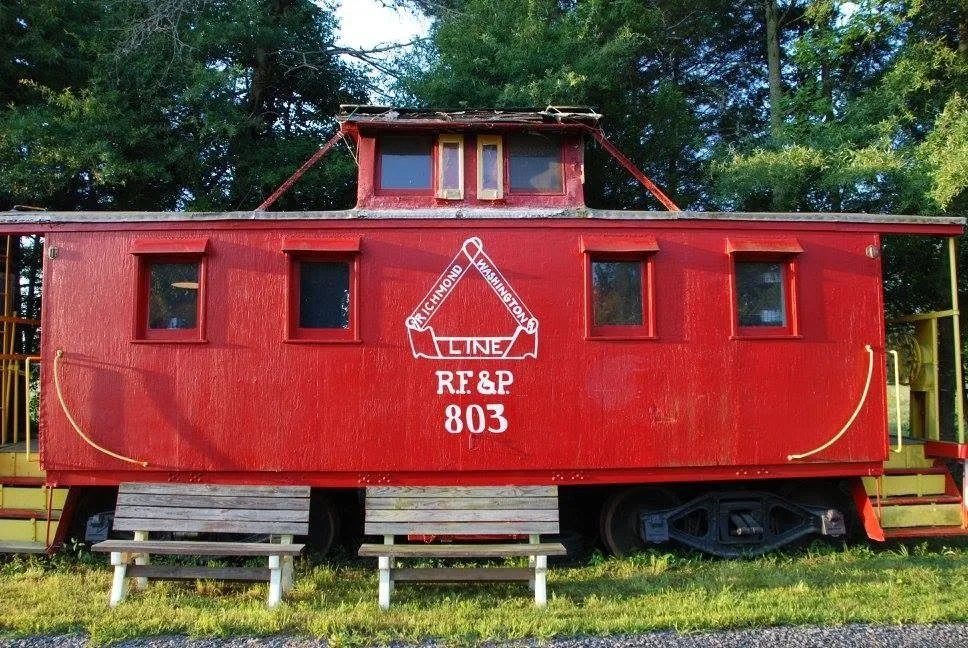 Restored red railroad caboose with Union Pacific logos and markings, located outdoors on grassy ground with trees in the background.