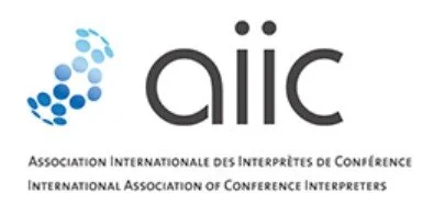 Logo der Internationalen Vereinigung der Konferenzdolmetscher mit grünen und blauen Kreisen und deutschem und englischem Text.