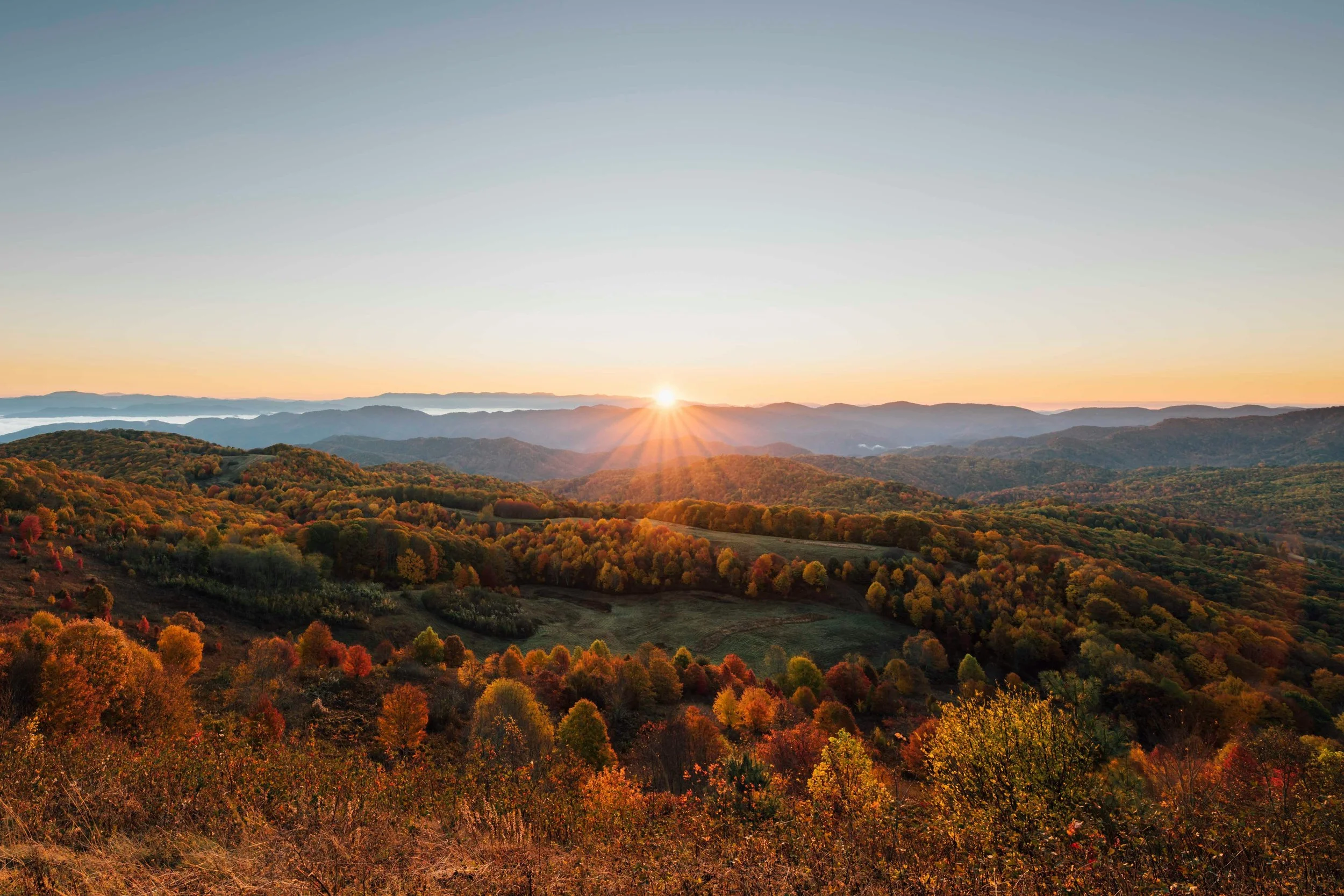Sunrise over a mountain range with colorful autumn trees in the foreground.