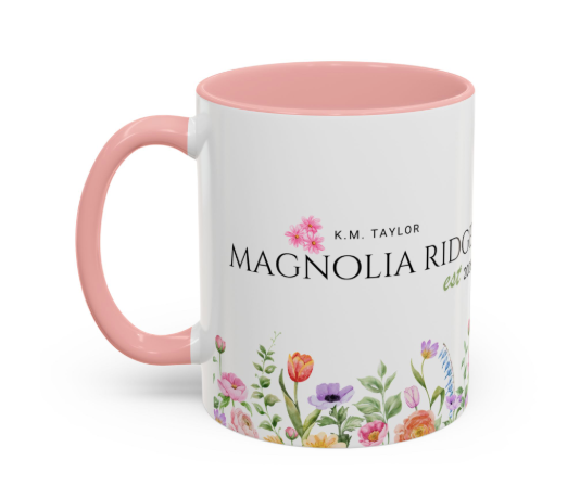 White ceramic mug with pink handle and interior, featuring colorful flowers at the bottom and the text 'K.M. Taylor Magnolia Ridge' on the side.