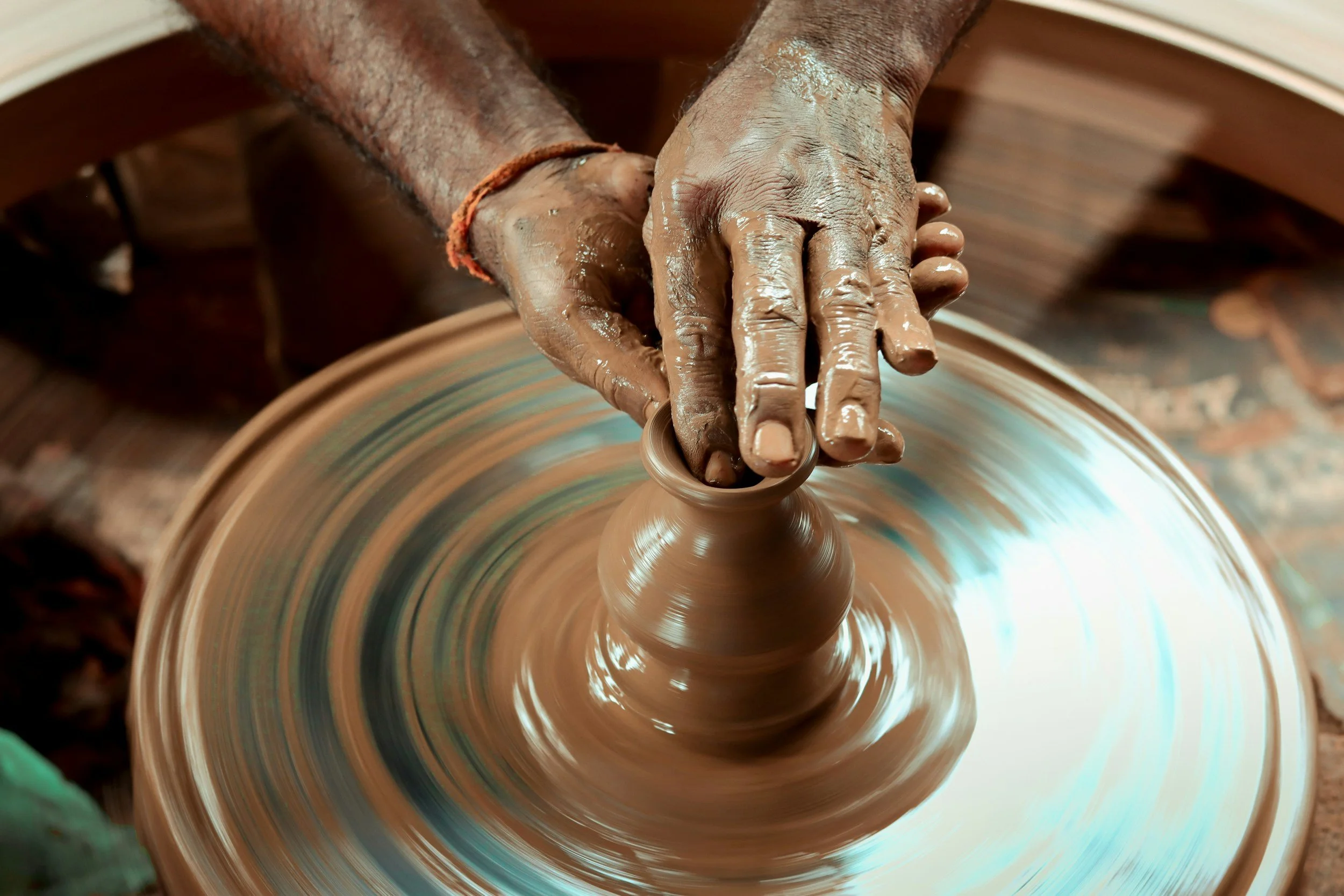 Close-up of hands shaping clay on a spinning pottery wheel, with wet clay on fingers and wheel surface.