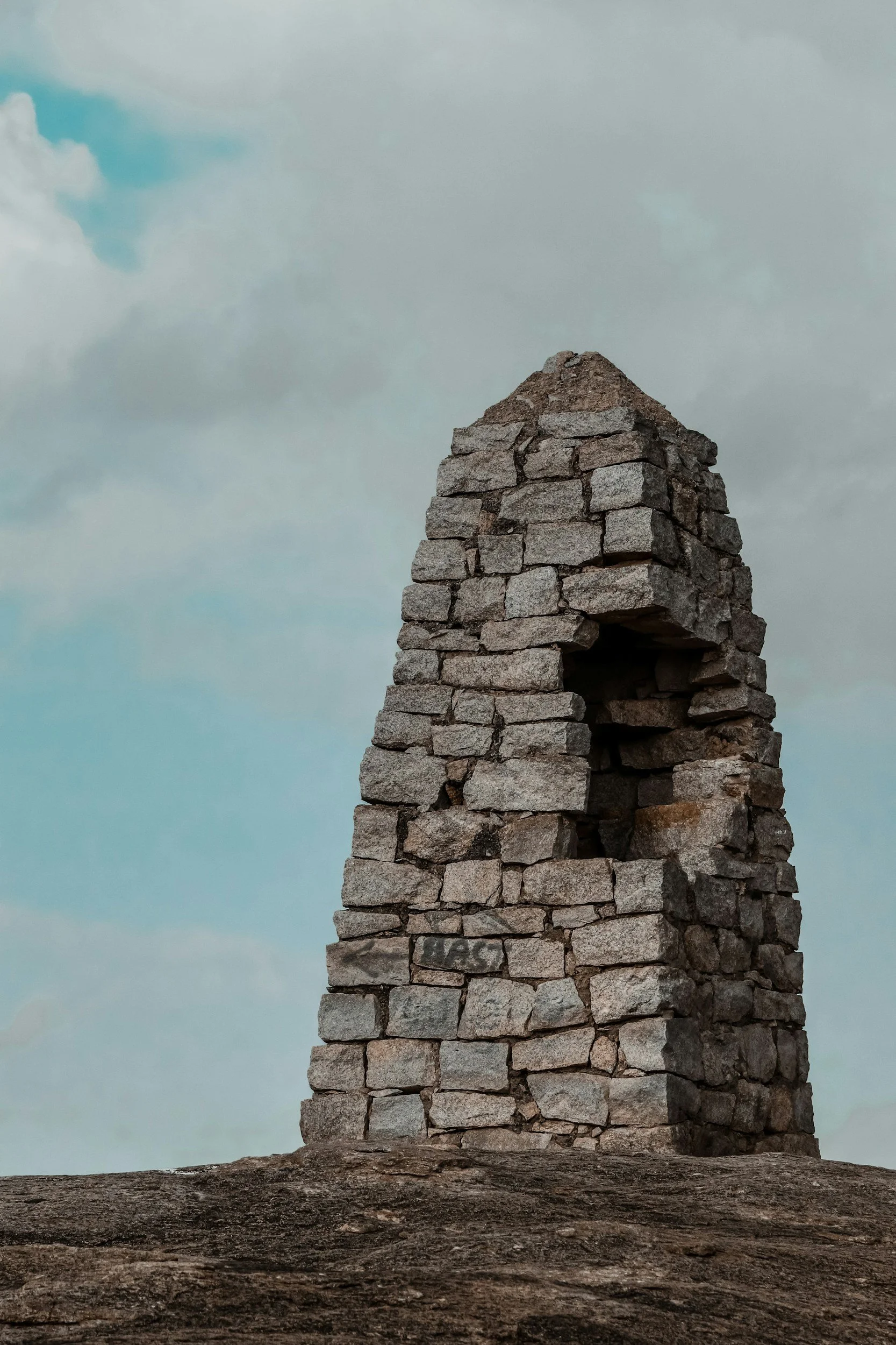 A stone structure made of stacked rocks, with a hole in the middle, against a cloudy sky.