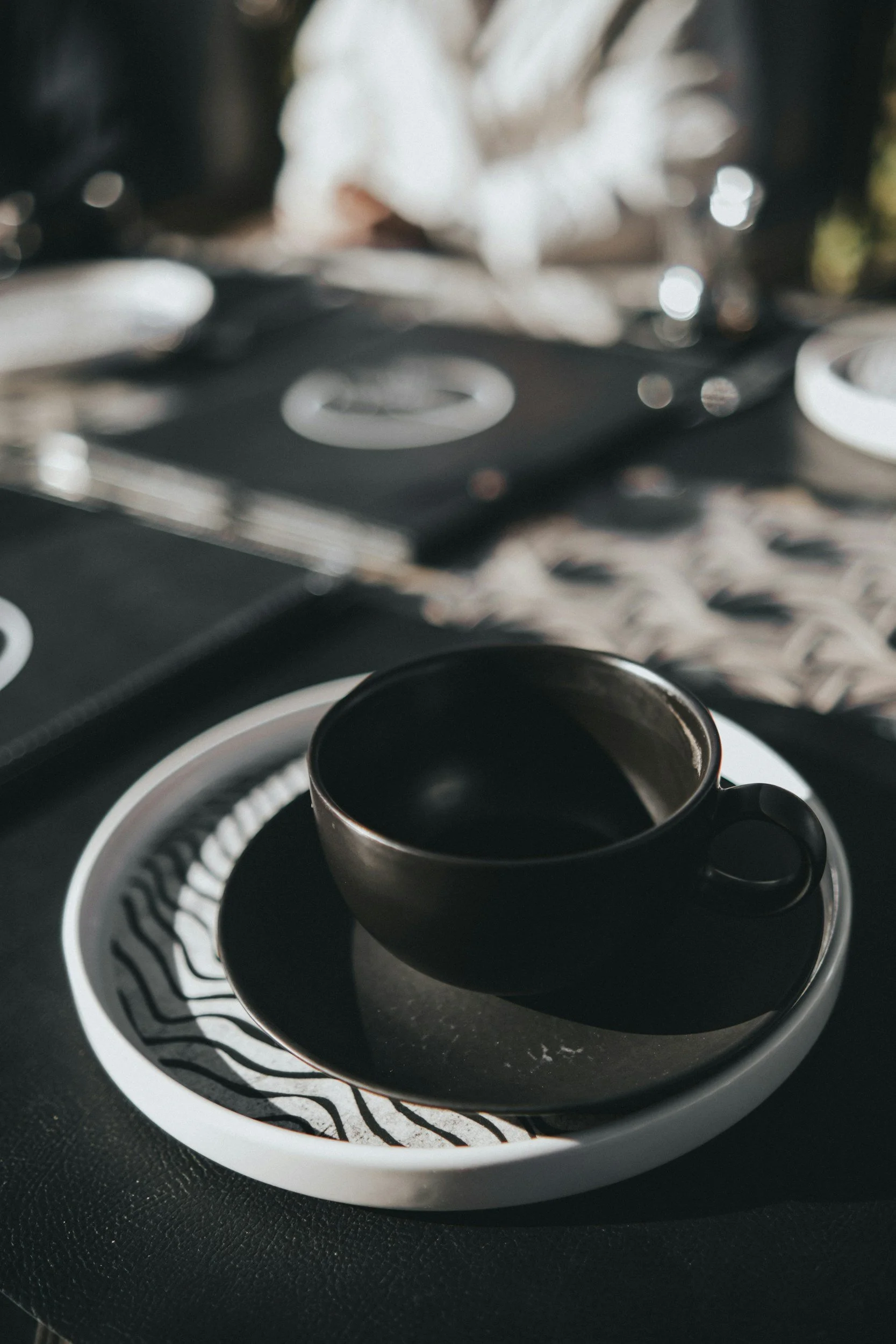 A close-up of a steaming cup of black coffee placed on a decorative black and white saucer, on a black textured surface.