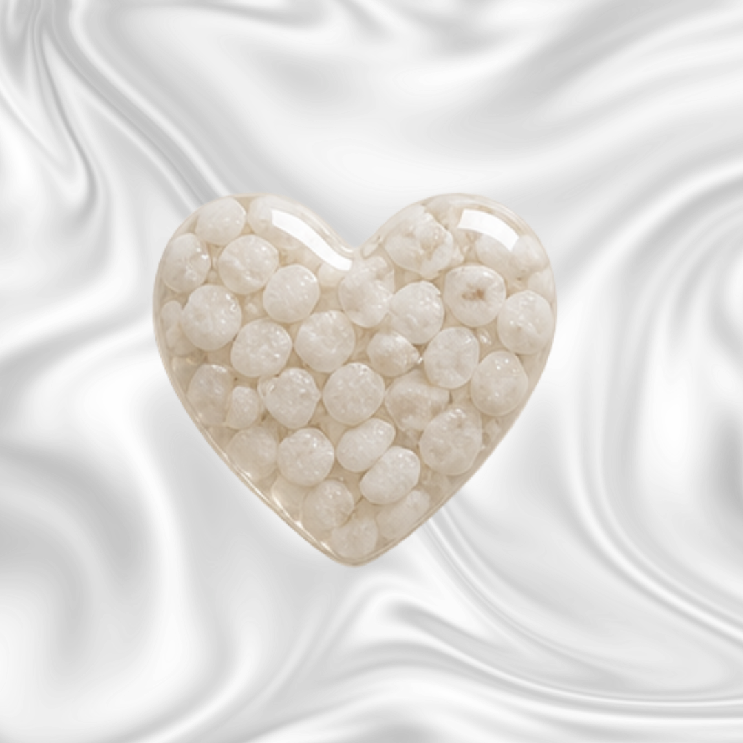 A heart-shaped object filled with white, round pearls or beads, set against a marbled black and gray background.