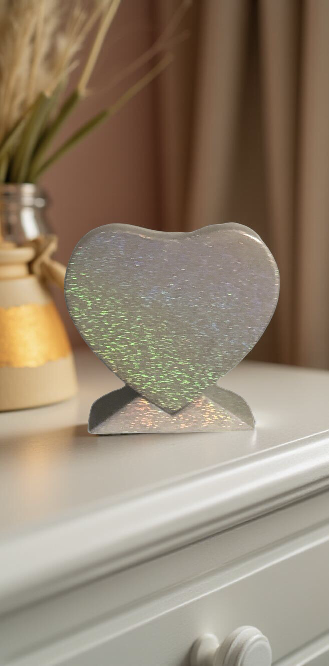 Decorative silver heart-shaped mirror on a white dresser with a vase of dried plants in the background.