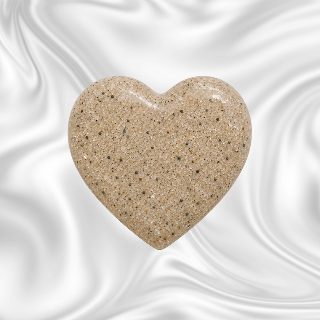 A heart-shaped object made of beige and black speckled sand against a dark, swirling background.