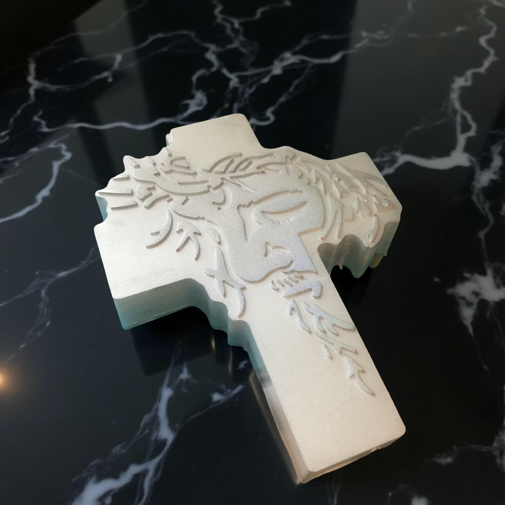 A metal cross with an engraved image of a lion's face on a black marble surface.