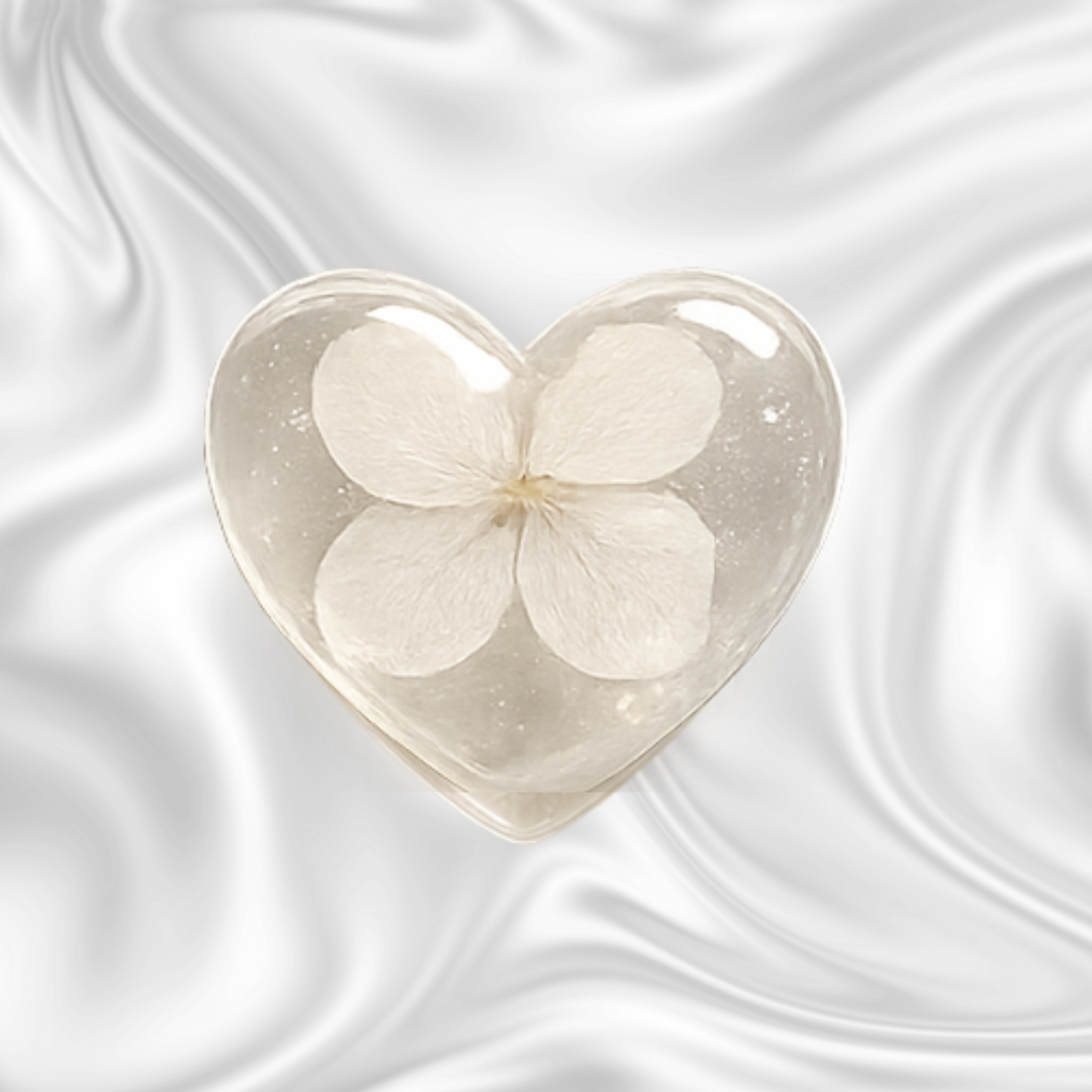 A clear heart-shaped soap with a white flower inside, set against a black and gray marbled background.