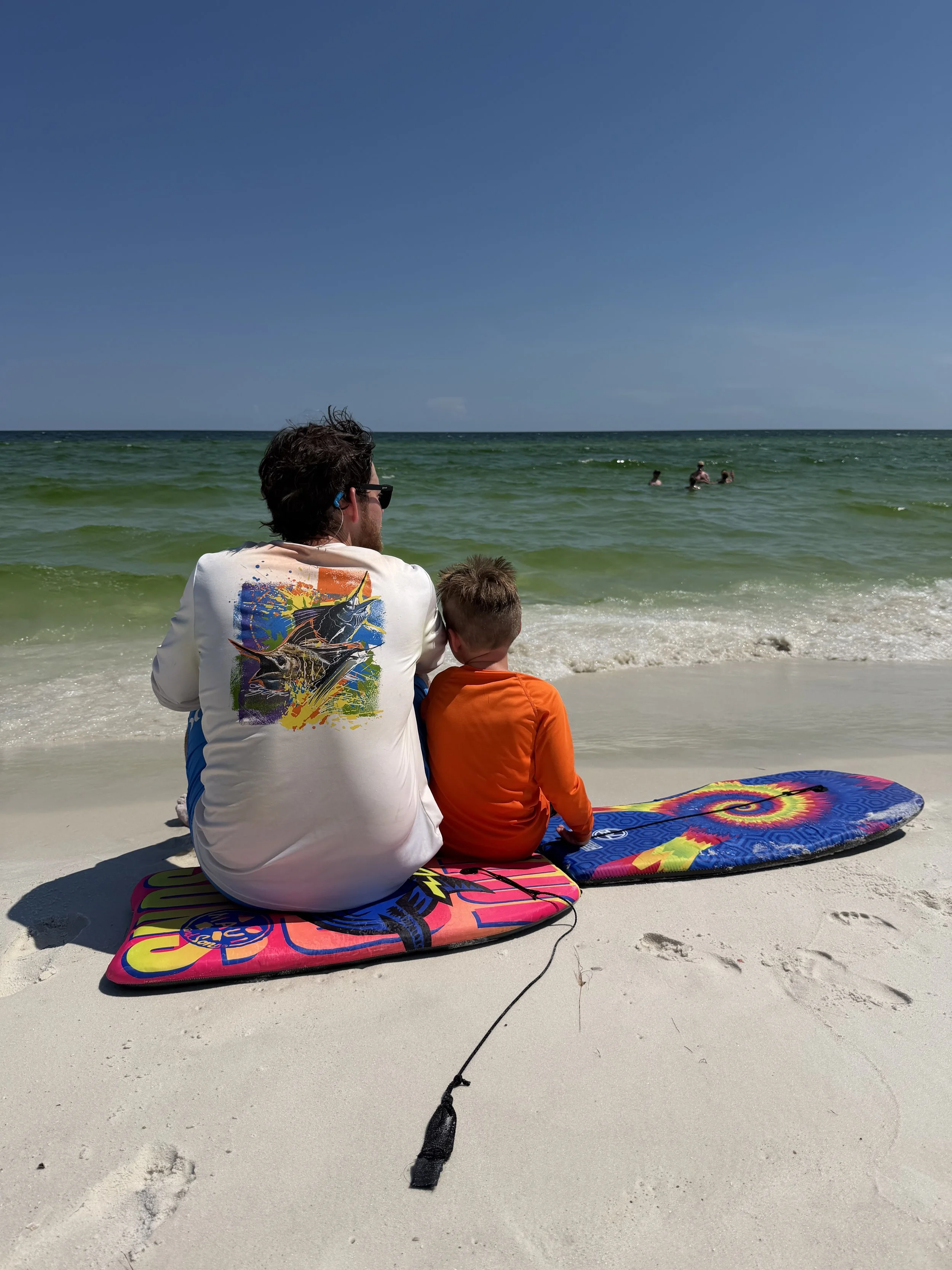 dad and son sitting on boogie boards on the beach