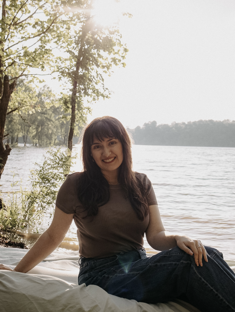 gvb marketing agency employee, Lillie Daniel, sitting outdoors near East Fork Lake with trees and warm sunlight behind her.