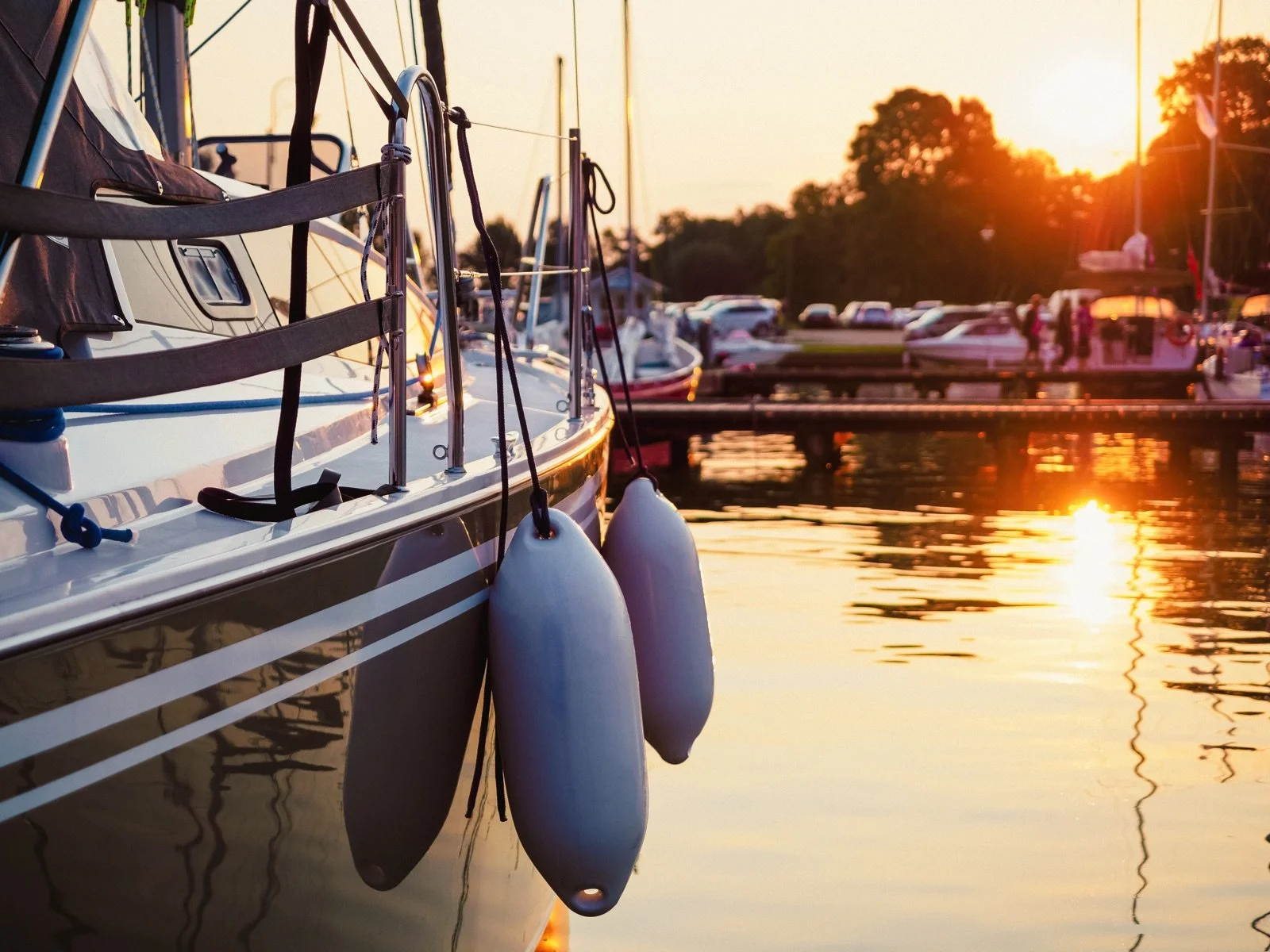 A sailboat moored at a dock at Up The Creek Marina, Bayville NJ during sunset, with reflections on the water and other boats in the background.