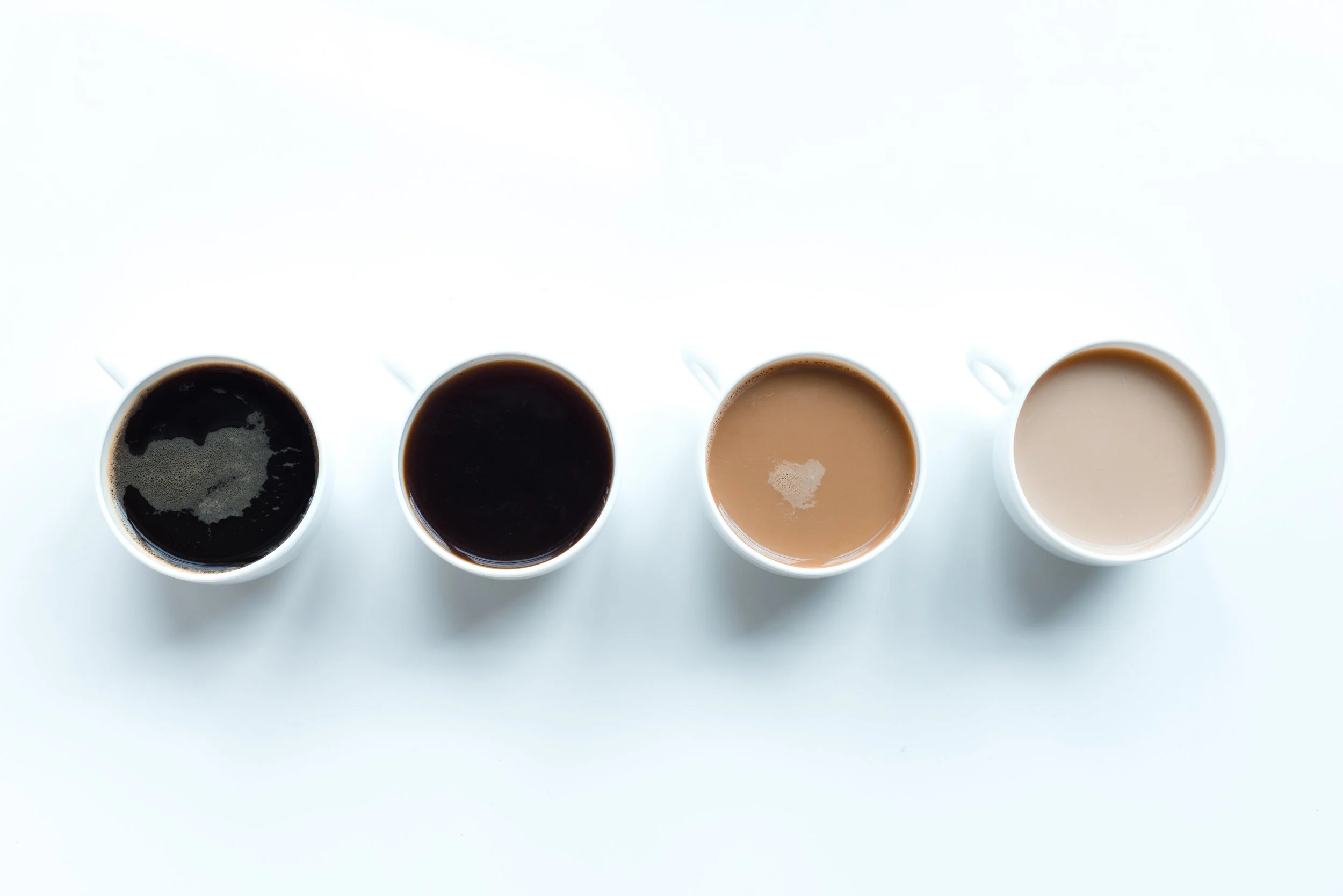 Four white cups filled with coffee, arranged in a row on a white background.