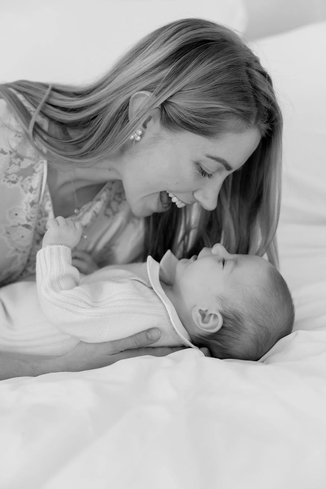 Black and white photo of a woman and a baby lying on a bed, smiling and touching noses.