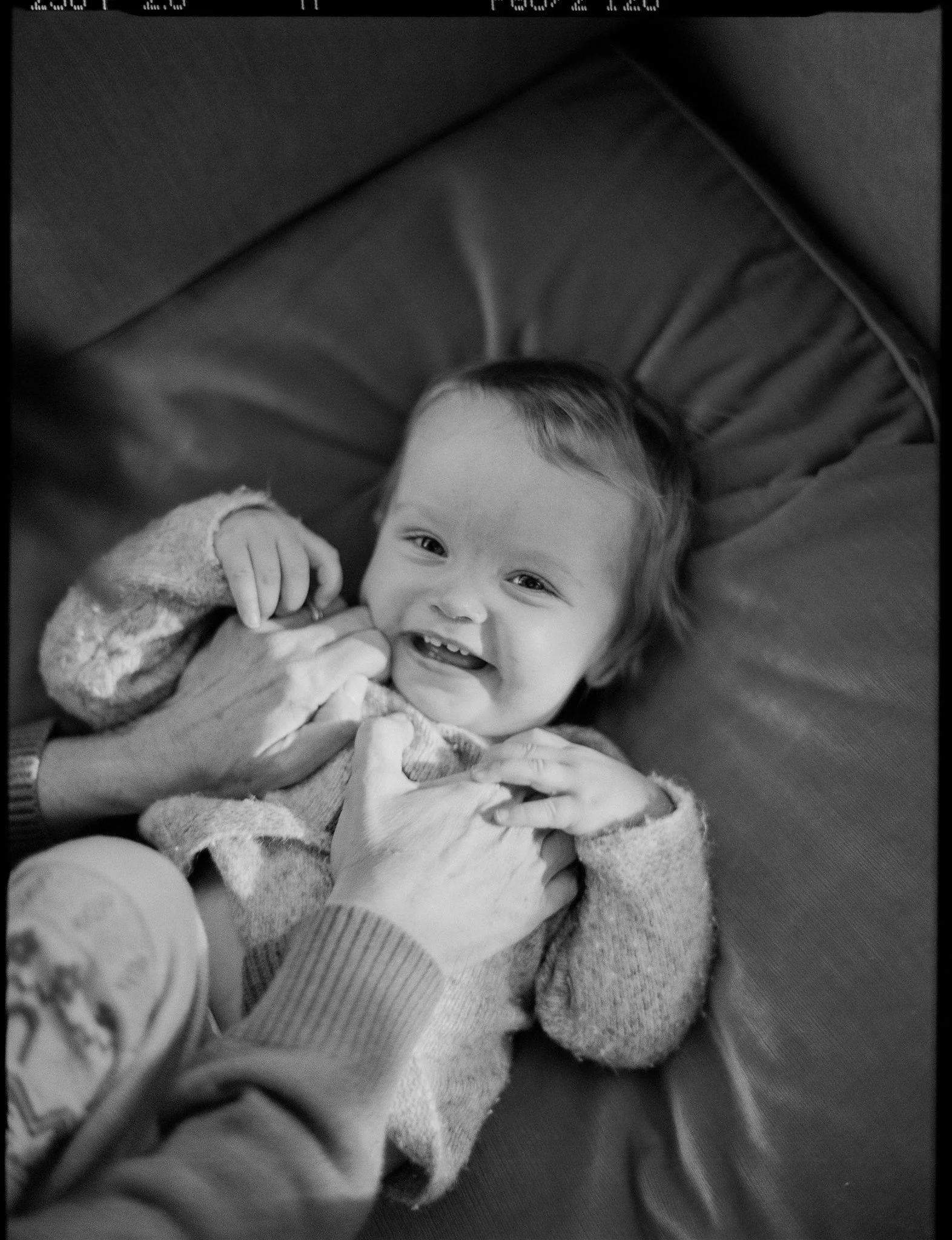 A young child lying on a bed, smiling at the camera, wearing pajamas with a soft fleece blanket covering part of their body, with a wooden headboard visible behind.