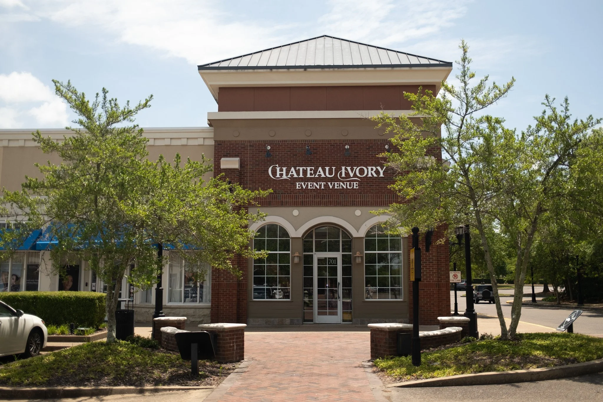 Exterior view of the Chateau NVORY Event Venue building with red brick and beige siding, large arched windows, and signage displaying the venue name.
