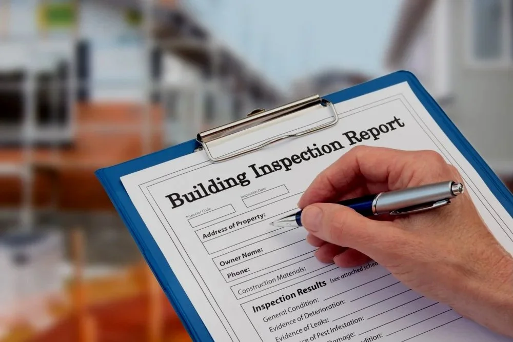 A person filling out a building inspection report on a blue clipboard.