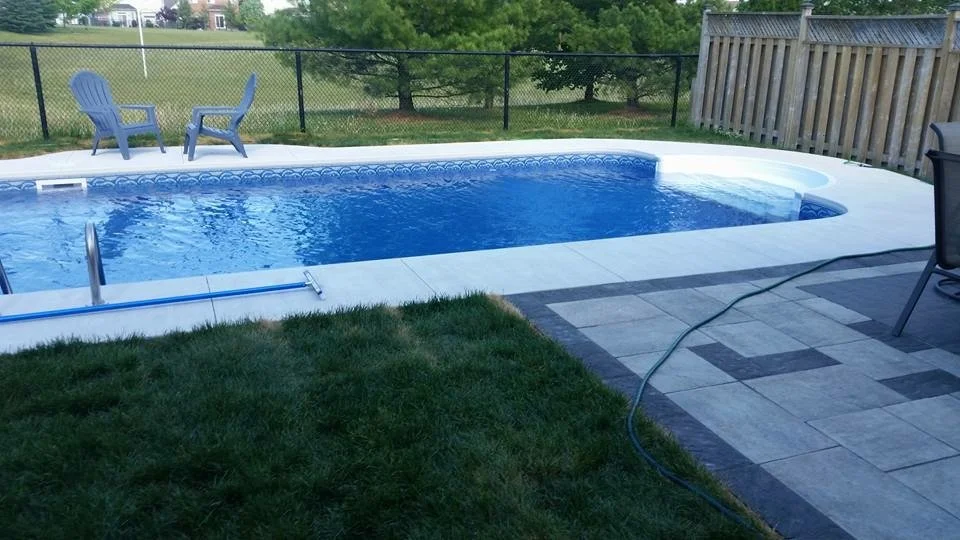 Backyard with in-ground swimming pool, two blue chairs on the grass, and a patio with tiled flooring surrounding the pool.
