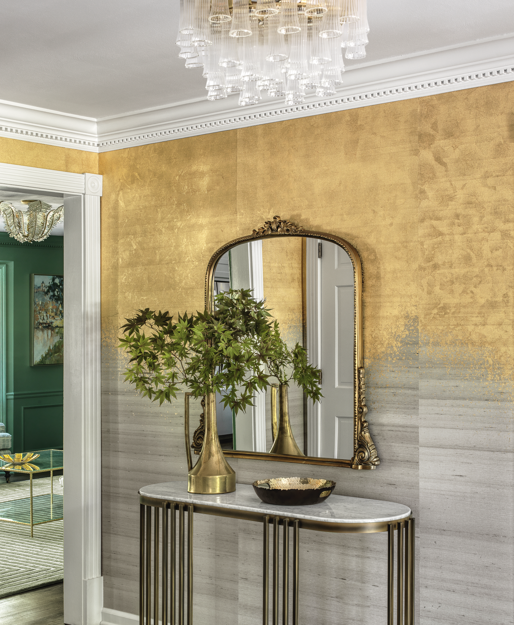 Entryway with gold wall, ornate mirror, marble-top console table, brass vases, decorative bowl, and chandelier.