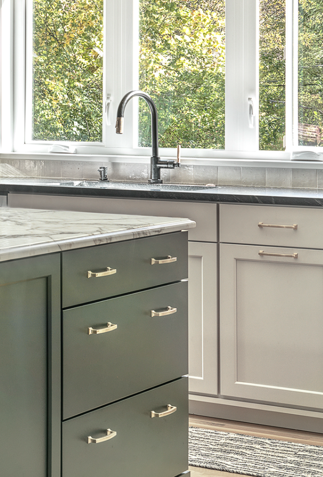 A modern kitchen with dark green cabinets, a marble island, and a window showing trees outside.