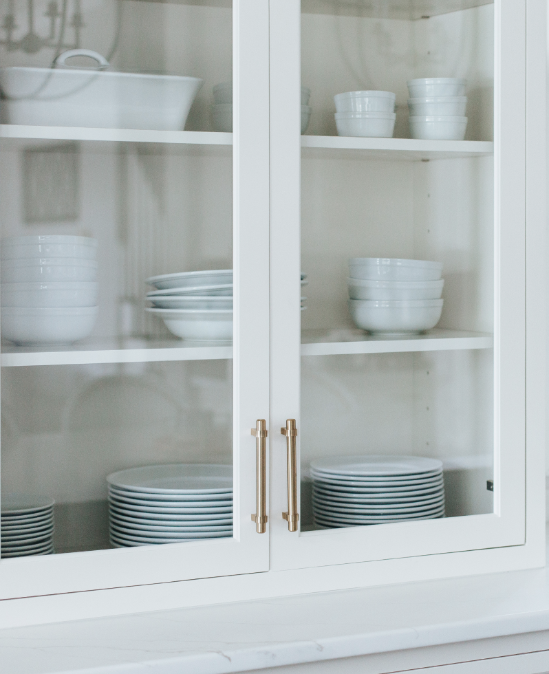 White kitchen cabinet with glass doors containing stacked white bowls and plates.