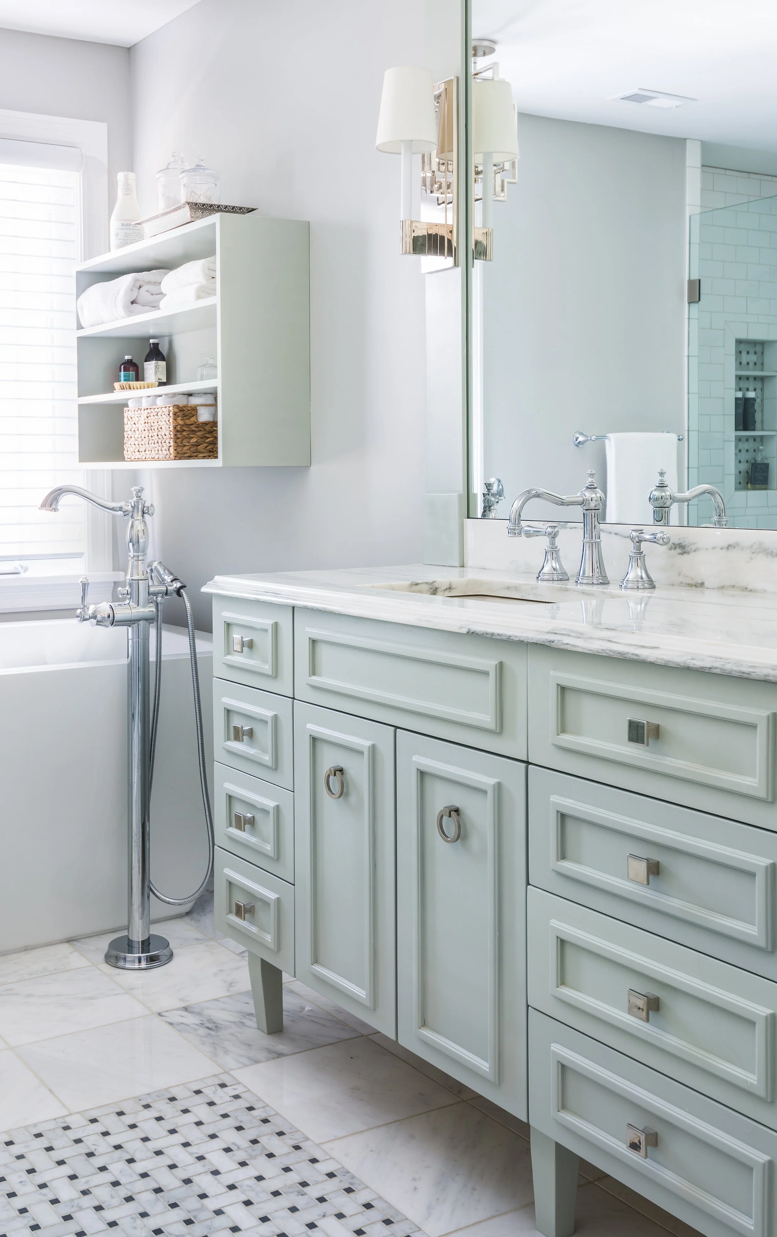 Bathroom with white walls, a mint green vanity with multiple drawers and white countertop, a large mirror, marble tile flooring, and a window.