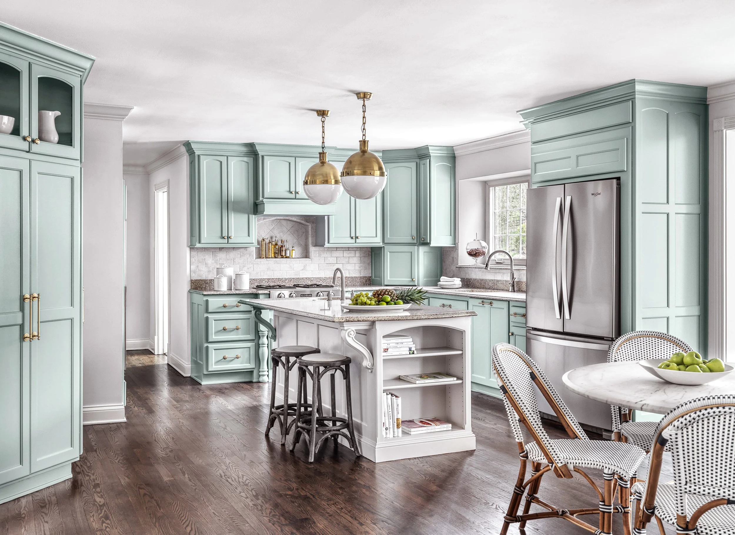 A kitchen with mint green cabinets, a kitchen island, pendant lights, and a round dining table with rattan chairs.