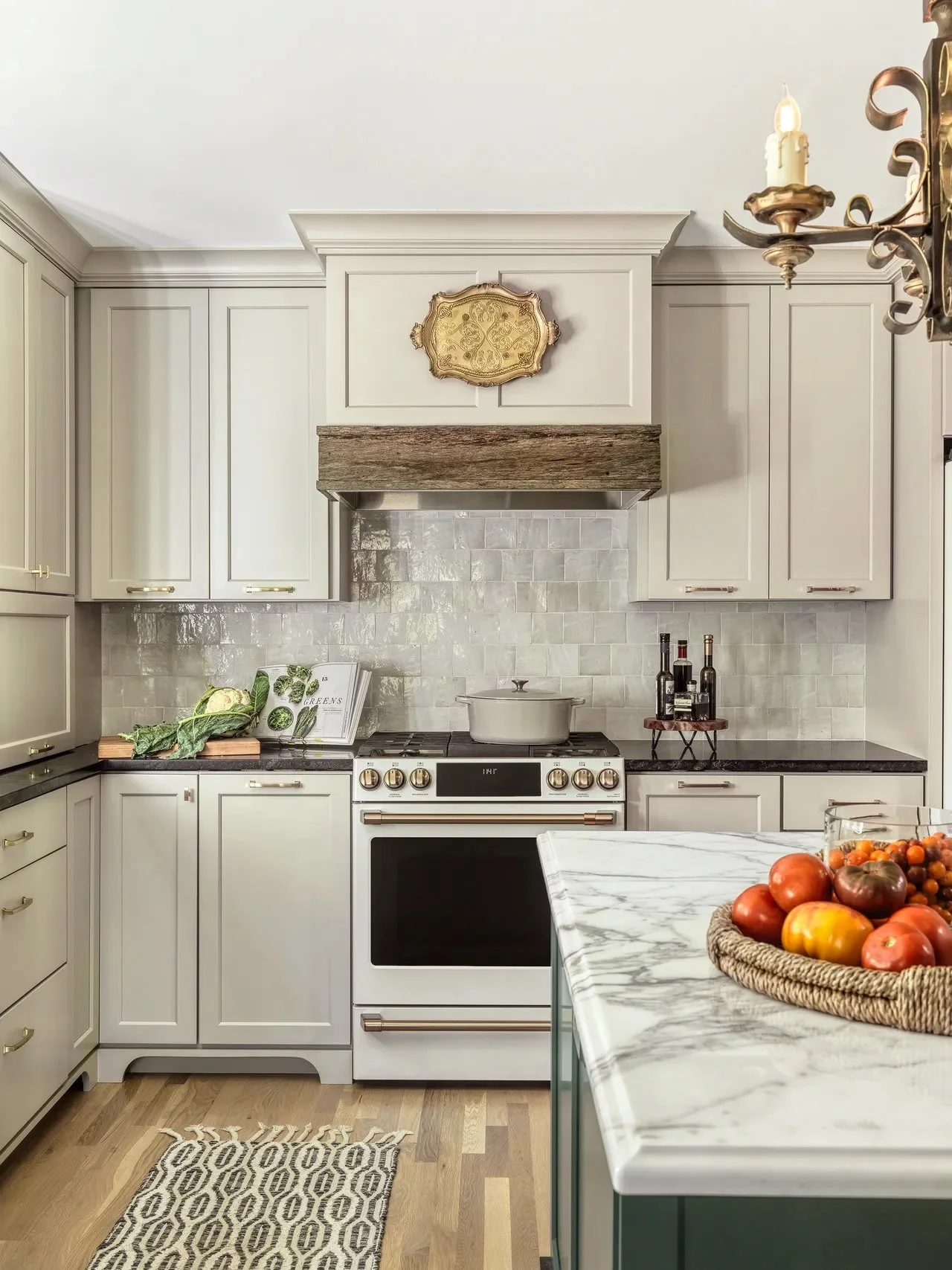 A modern kitchen with white cabinets, a gas stove and a marble countertop. A decorative gold hanging lives on the range hood.
