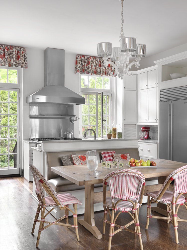 Bright kitchen with white cabinetry, stainless steel appliances, a wooden dining table with four chairs, and a chandelier.