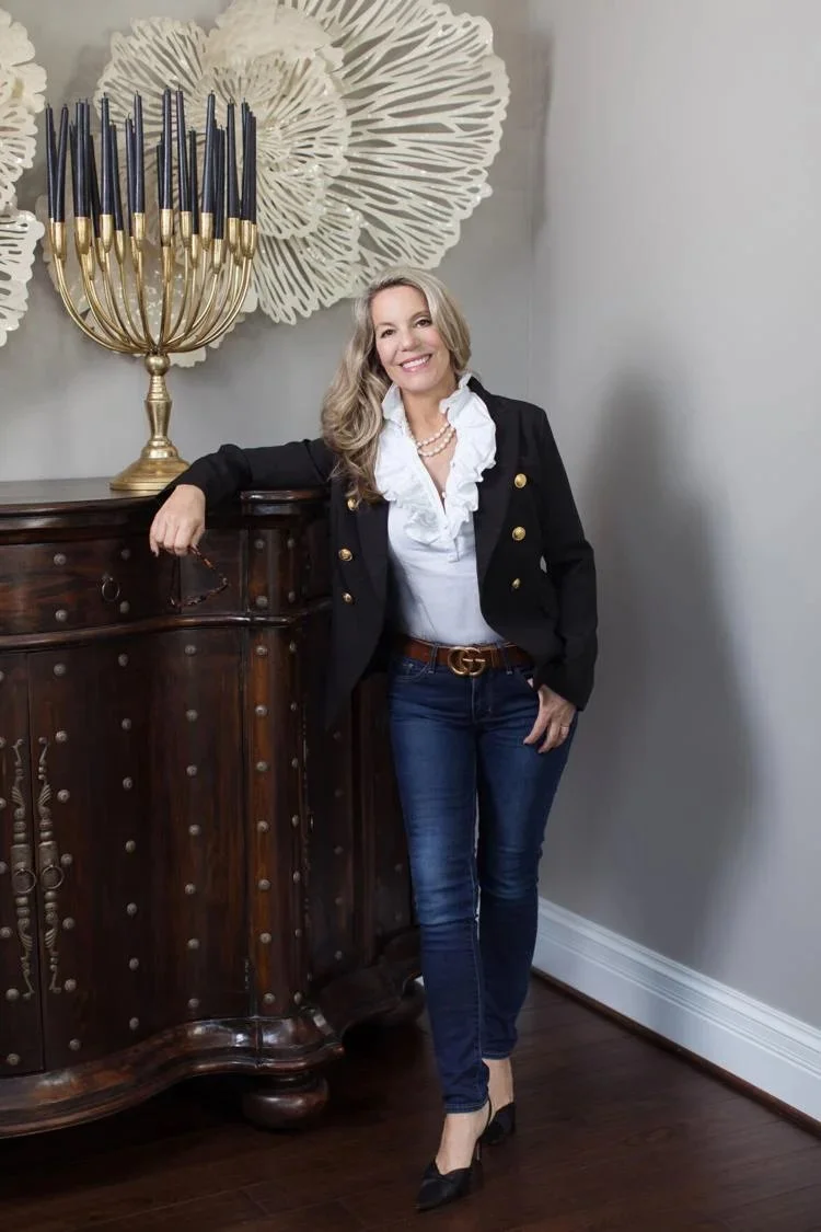Portrait of designer Joni Spear smiling, leaning on an armoire with a large candelabra alongside.