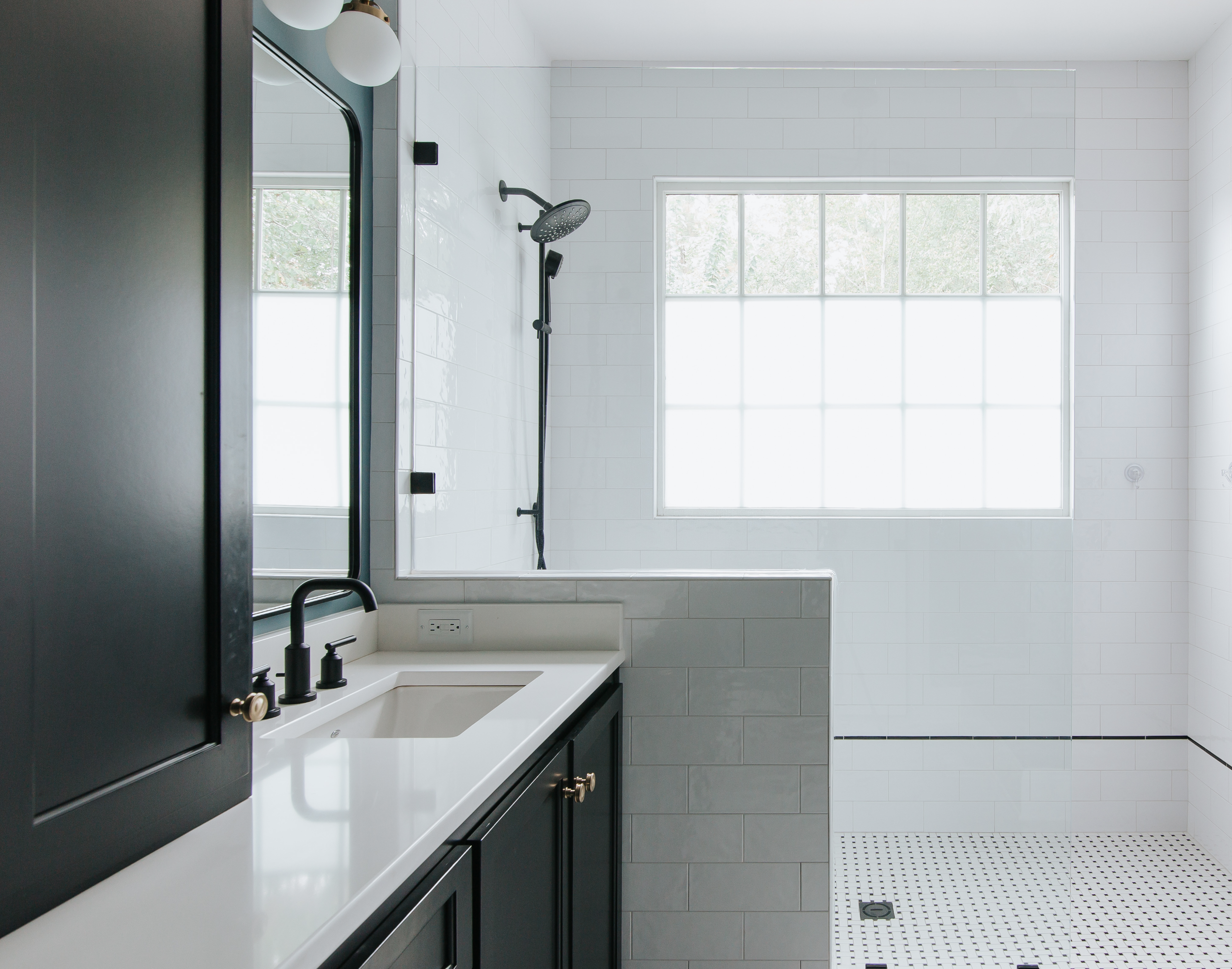 Modern bathroom with a black vanity, white countertop, matte black fixtures, large window and a shower area with a rain showerhead.