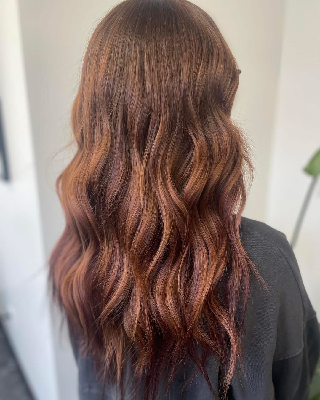 Back view of a person with long, wavy hair dyed in shades of brown and red.