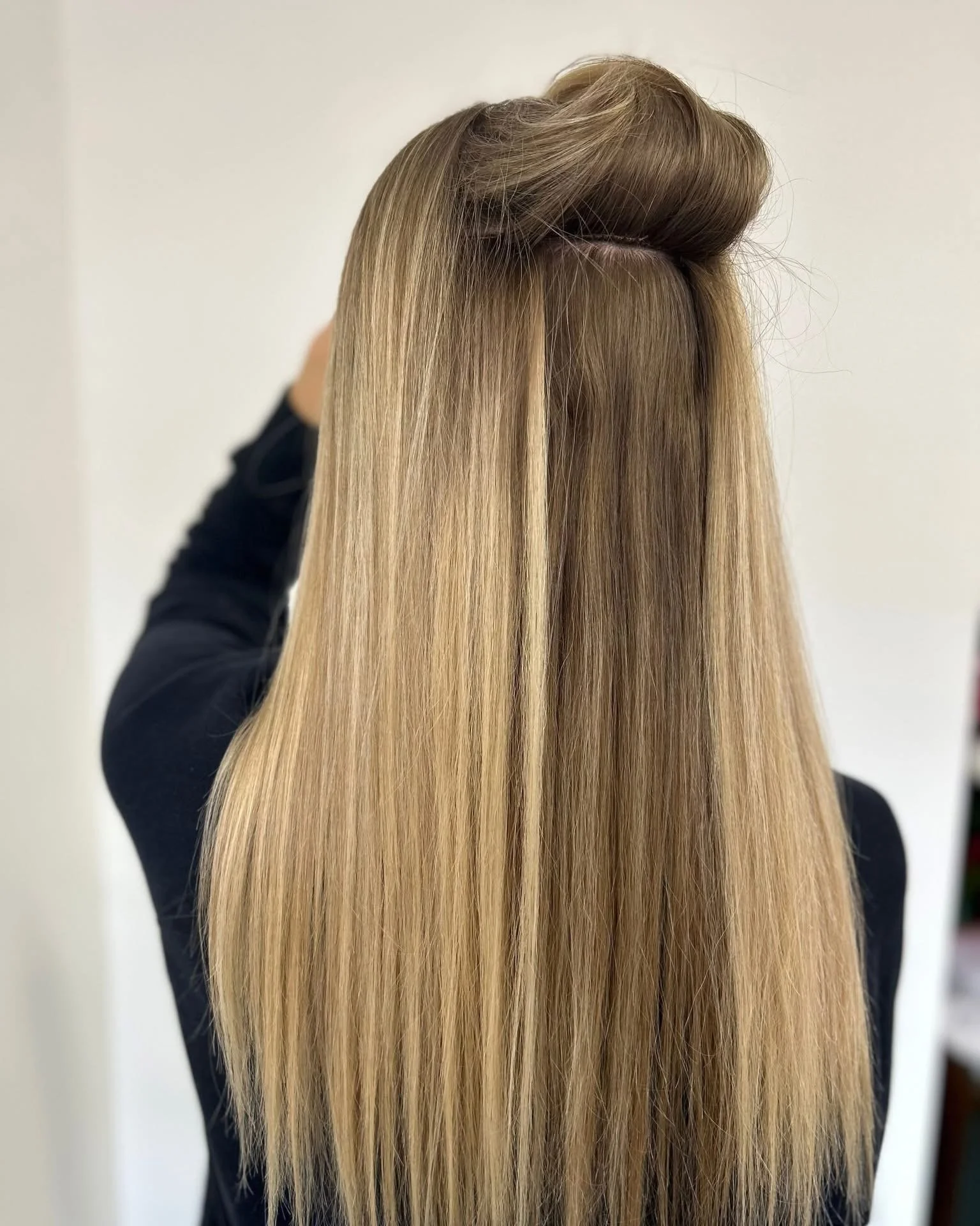 Close-up of long, straight, blonde hair with a section styled into a roll at the crown, seen from the back.