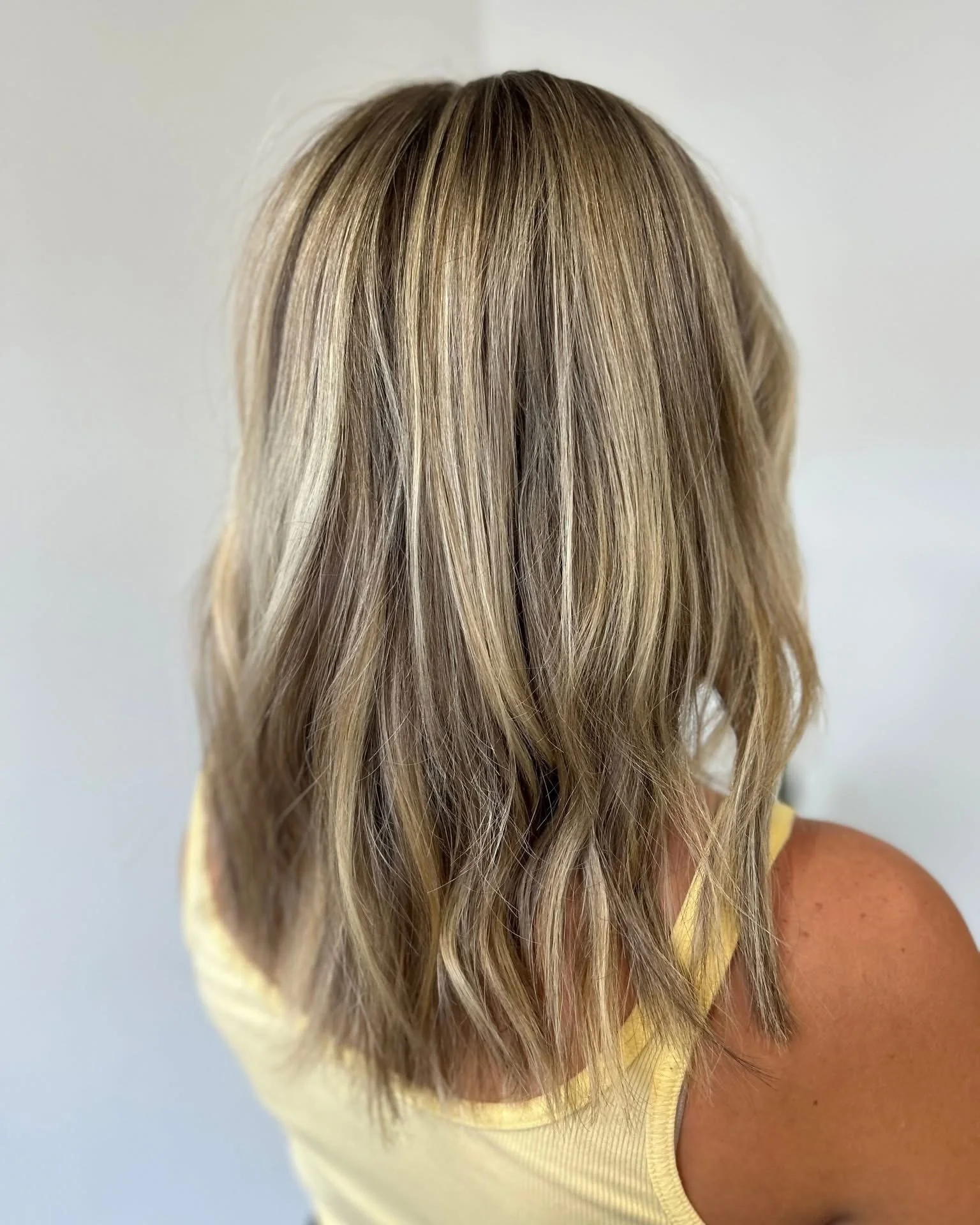 Back view of a woman with long, wavy blonde hair wearing a sleeveless yellow top.