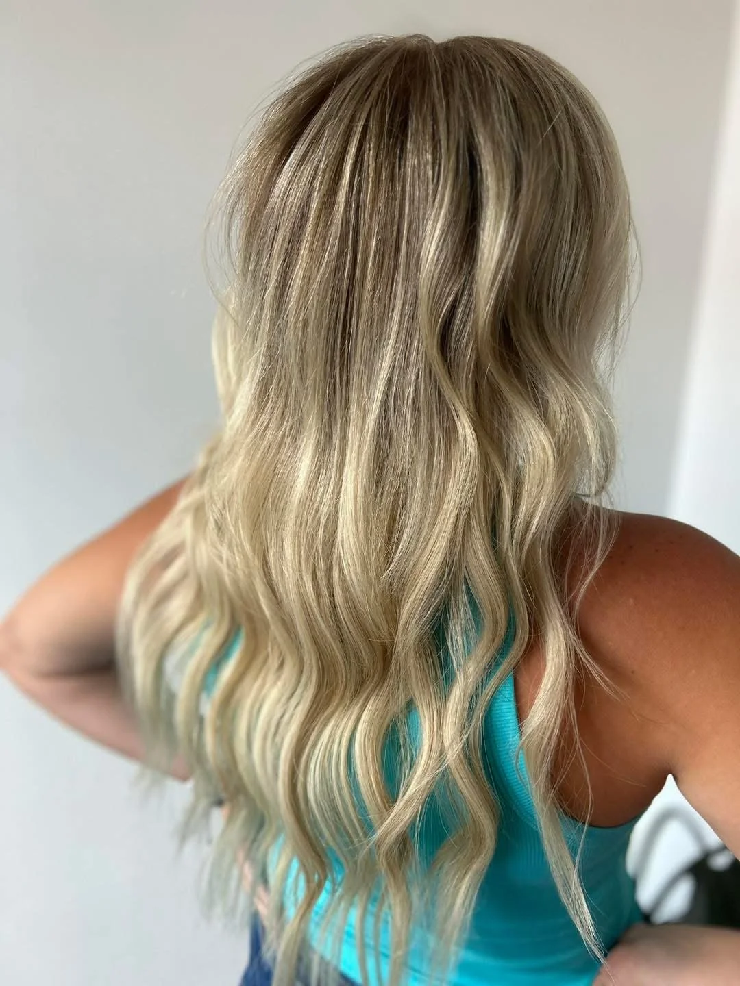 Woman with long, blonde, wavy hair viewed from behind, wearing a turquoise top.