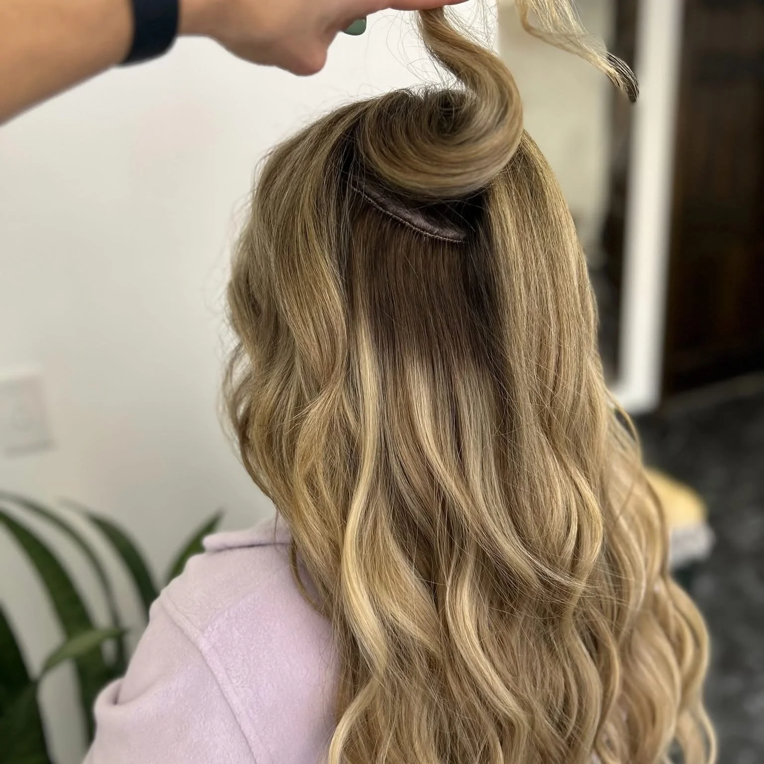 A person with blonde, wavy hair having a hair extension or styling process done at a salon.