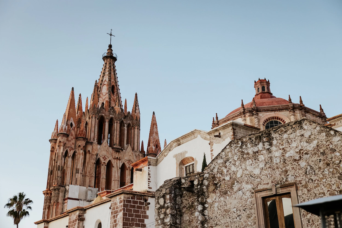 A historic Gothic-style church with intricate spires and a weather vane on top, set against a clear sky.