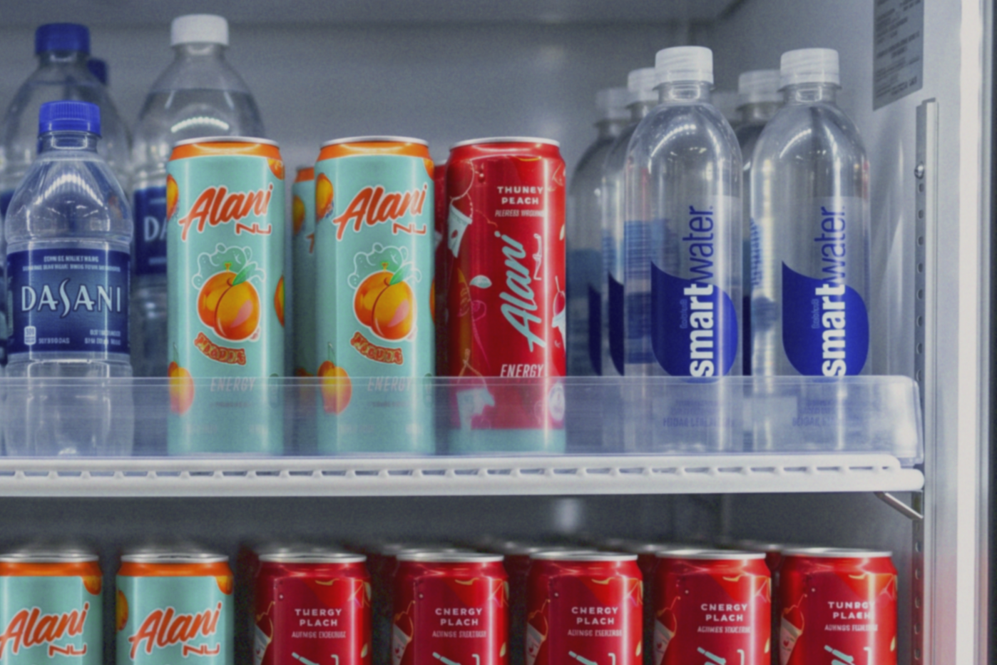A refrigerator shelf with bottles of Dasani water, canned Alani Nu energy drinks, and cans of Alani Energy drinks.